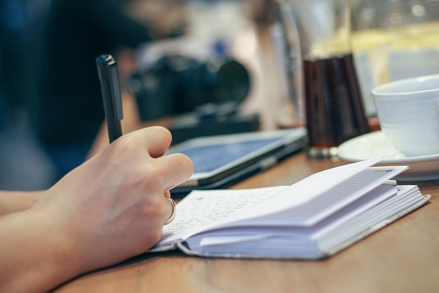 Homme qui écrit dans un livre avec un crayon tenu dans sa main droite.