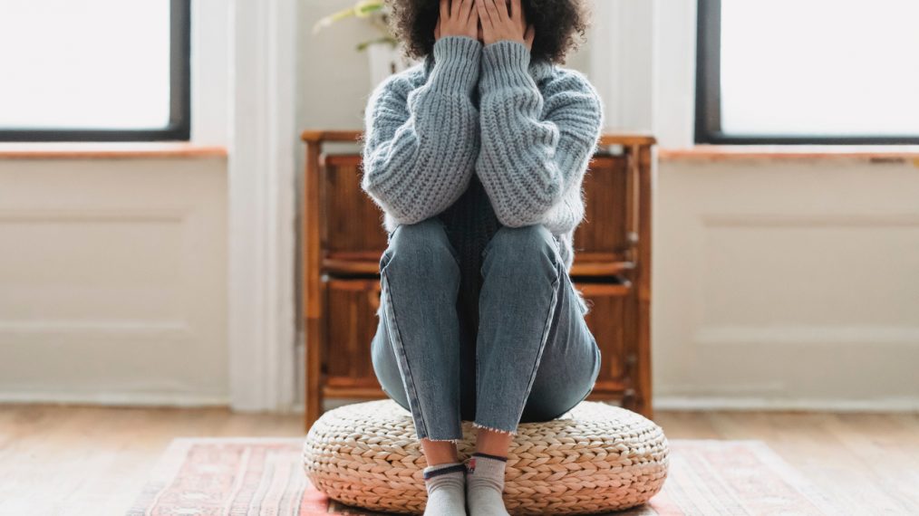 Une femme est assises sur un pouf et se prend la tête dans les mains.