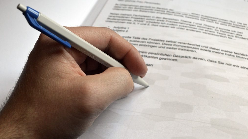 Quelqu'un écrit avec un stylo sur une lettre de motivation tapuscrite (sûrement pour la signature manuscrite)