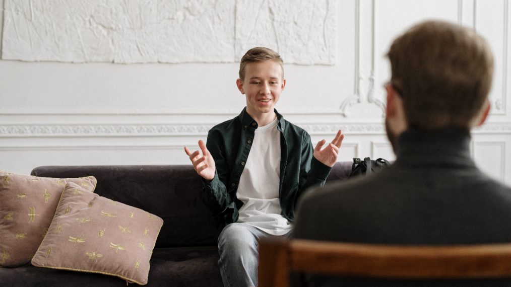 On voit un enfant dans un salon. Il est face à un adulte et semble lui parler.