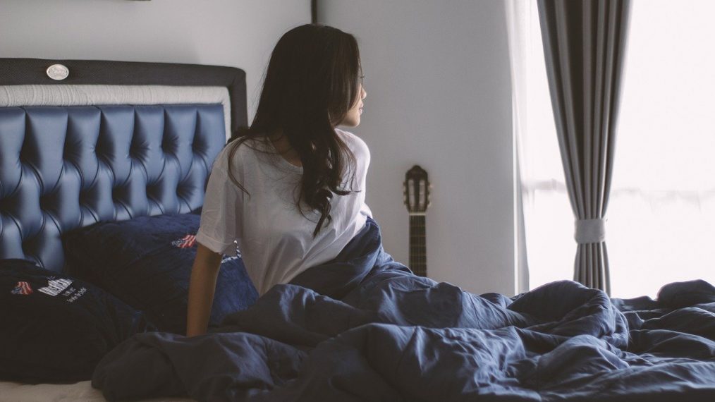 Une femme se lève de son lit et regarde par la fenêtre.