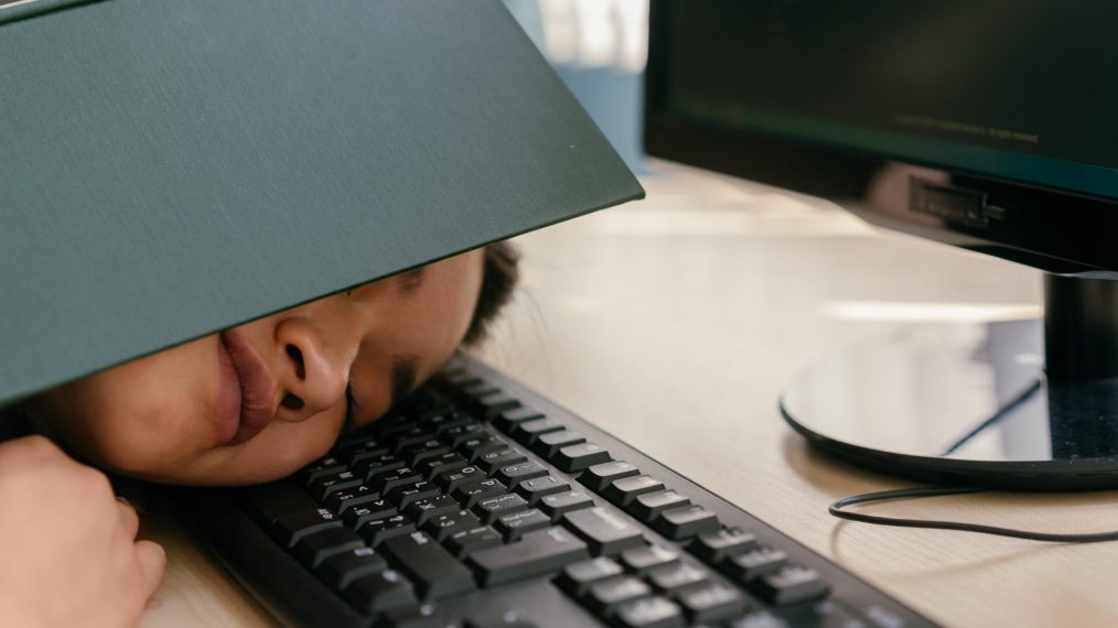 Une jeune fille est allongée sur le clavier d'un ordinateur et sa tête est recouverte d'un livre ouvert.