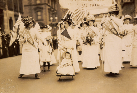 Un défilé des suffragettes dans la rue avec un enfant dans une poussette.