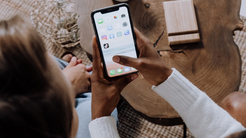 Deux personnes sont assises. L'une d'elle tient un téléphone dans la main et montre du doigt l'application TikTok.